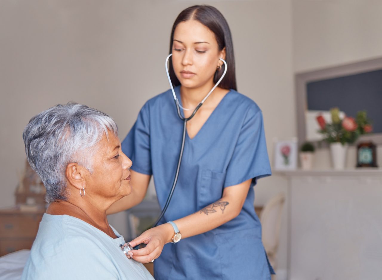 A nurse using a stethoscope to check the heartbeat of an elderly woman in a calm, professional setting.