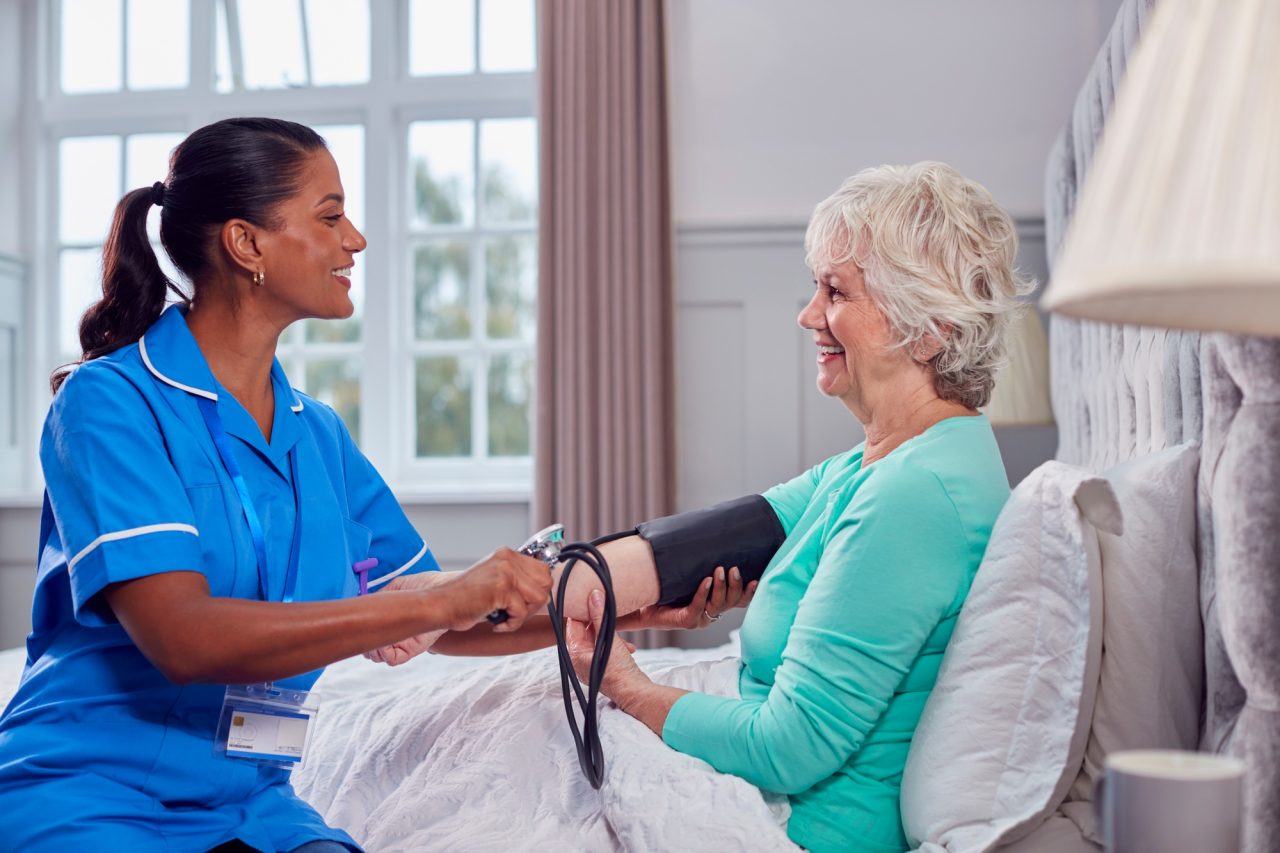 A nurse measuring the blood pressure of an elderly woman in a bright and comfortable bedroom.