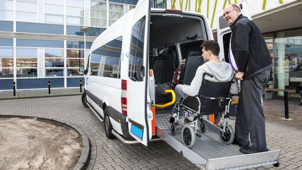 A man in a wheelchair being assisted into a van by a caregiver using a wheelchair ramp.